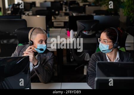 Due donne in maschere mediche lavorano in ufficio. Operatori di call center femminili Foto Stock