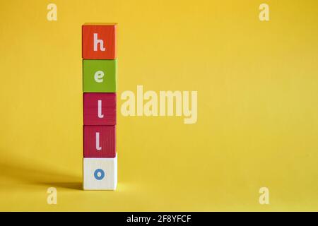 Parola Ciao fatto di blocchi di legno colorati. I cubi dipinti con lettere sono disposti verticalmente su sfondo giallo. Vista dall'alto. Spazio di copia Foto Stock