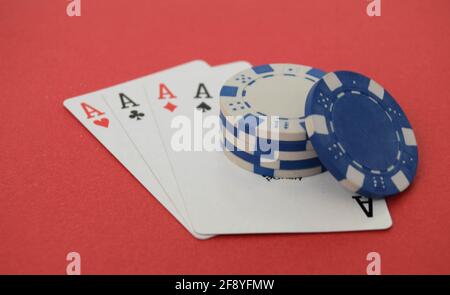 Una mano vincente di quattro assi e chip di poker su sfondo rosso.