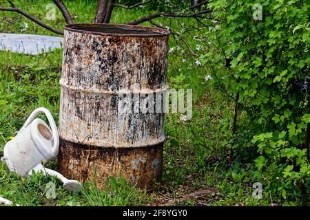 un vecchio barile di ferro si trova tra gli alberi, nel giardino Foto Stock