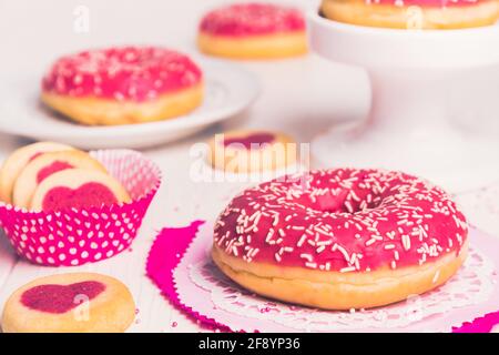 Ciambella smaltata rosa su bianco, decorata con biscotti e altre ciambelle sullo sfondo Foto Stock
