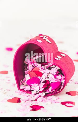 I piccoli cuori rossi, rosa e bianchi per la decorazione versano da una piccola scatola a forma di cuore. Verticale con spazio per la copia. Foto Stock