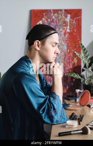Giovane seduto al tavolo con cosmetici e preparazione per le sue prestazioni Foto Stock