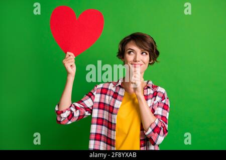 Foto di una persona intelligente che guarda vuoto spazio tenere la mano camicia a forma di cuore isolata su sfondo di colore verde Foto Stock