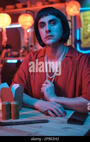 Ritratto di giovani transgender guardando la fotocamera mentre si è seduti a. il tavolo nel nightclub Foto Stock