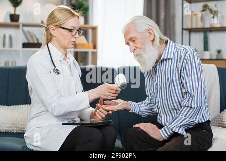 Misurazione della temperatura corporea. Termometro laser a infrarossi senza contatto. Donna medico tiene il termometro pronto per misurare la temperatura corporea del suo paziente anziano maschio a casa. Foto Stock