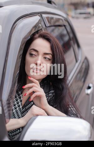 una donna favolosa in un'automobile che indossa un vestito a scacchi che si stacca fuori dalla finestra dell'automobile. bruna attraente in automobile Foto Stock