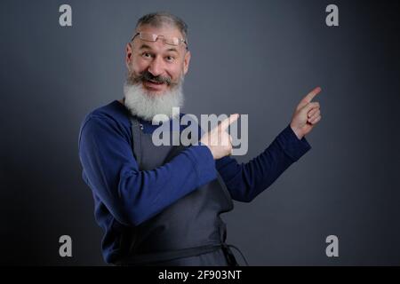 Seguimi. Guardate qui. Primo piano ritratto di allegro felice qualificato esperto gioioso grembiule-indossando nonno che indica su vuoto posto sopra Foto Stock