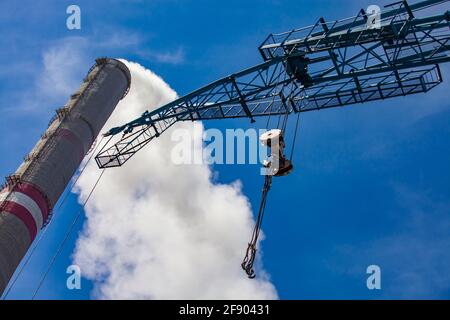 Tetto della centrale termica GRES-1. Primo piano del braccio della gru con ganci e fumatore con fumo. Cielo blu. Foto astratta. Ekibastuz, Kazakistan. Foto Stock