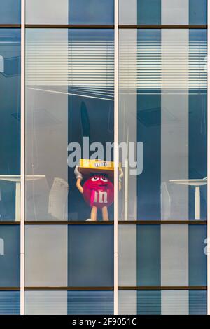 La grande figura rossa di M's da solo in un edificio vuoto durante la pandemia del virus corona. Questa è la mascotte di carattere del cioccolato marca m&m's prodotto Foto Stock
