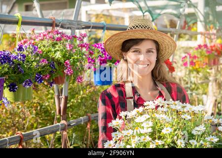 Ritratto di una donna sorridente lavoratrice vivaio serra con fiori in primavera Foto Stock