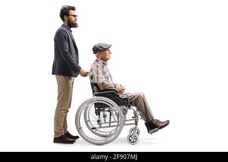 Foto di profilo a tutta lunghezza di un uomo bearded che lo spinge anziano padre seduto in una sedia a rotelle isolato su sfondo bianco Foto Stock