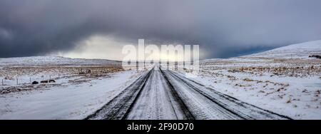 Strada coperta di neve dritta e paesaggio arido in inverno, Islanda Foto Stock