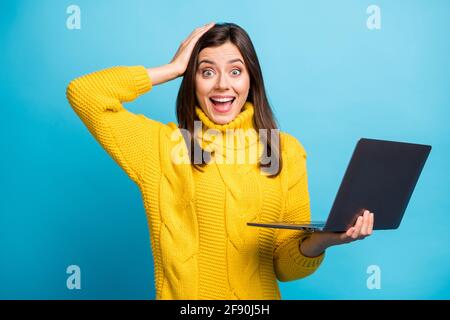 Ritratto di bella ragazza allegra stupita che tiene in mano il computer portatile grande successo isolato su sfondo di colore blu brillante Foto Stock