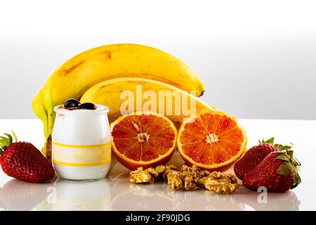 Bicchiere di latte con noci e frutta su un tavolo di vetro per una colazione isolato su bianco Foto Stock