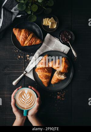 Mani che tengono il latte accanto ai croissant sul tavolo nero dall'alto. Foto Stock