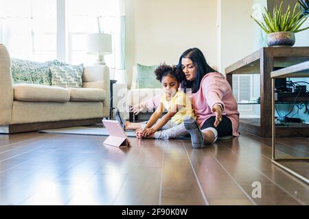 Ragazza che pratica yoga con nonna durante la lezione di esercizio online a. casa Foto Stock