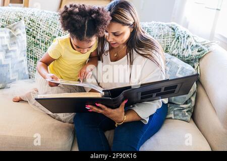 Madre e figlia che guardano un album fotografico mentre si siedono divano a casa Foto Stock