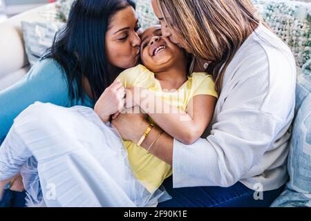 Nonna e madre baciando una ragazza sorridente sul divano a casa Foto Stock