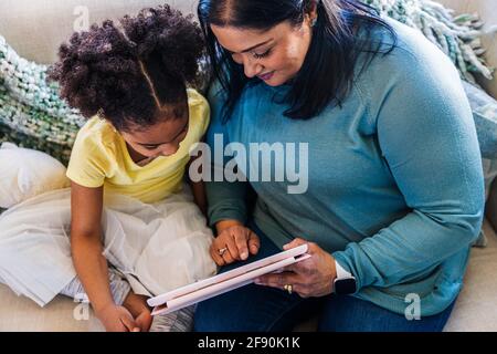 Nonna che mostra il tablet digitale alla nipote mentre si passa il tempo libero insieme a casa Foto Stock