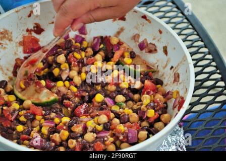 mescolare a mano fagioli neri freschi e insalata di mais in un ampia ciotola da portata Foto Stock