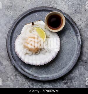 Sashimi vivi al capesante su conchiglia con salsa di daikon, lime e soia su sfondo grigio Foto Stock