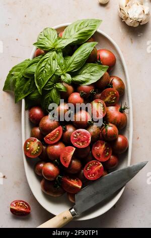 Pomodori ciliegini interi e affettati in una ciotola con basilico e spicchi d'aglio.