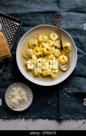 Tortellini fatti in casa in brodo con formaggio grattugiato su un blu tovagliolo Foto Stock