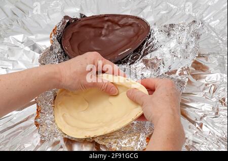 Uovo di Pasqua - le mani rompendo uovo di cioccolato farcito fatto in casa. Vista dall'alto. Spazio di copia. Foto Stock