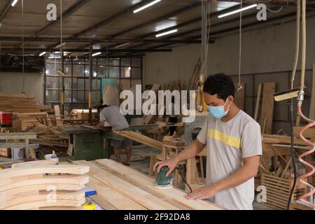 Carpentiere giovane in maschera facciale che lavora con una levigatura macchina Foto Stock