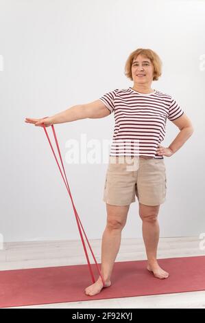 Una donna anziana è impegnata in forma fisica con un elastico banda su sfondo bianco Foto Stock