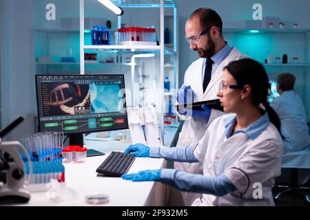 Team di ricercatori che lavorano in laboratorio scientifico, biochimica analisi dei dati campione su computer. Medici specialisti che discutono di trattamento innovativo utilizzando attrezzature ad alta tecnologia per l'assistenza sanitaria. Foto Stock