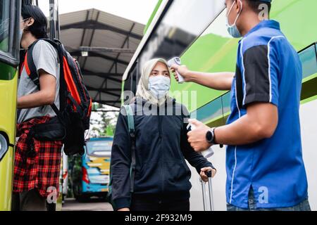 un uomo in una uniforme e un cappuccio usando un la pistola termica ispeziona il passeggero di una donna in un copricapo e maschera Foto Stock