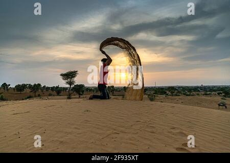 uomo non identificato gettando con sabbia nell'aria al deserto del thar jaisalmer, rajasthan. Foto Stock