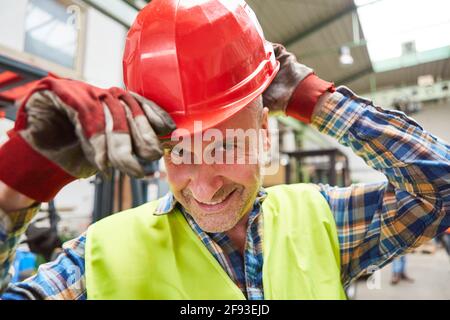 Sorridente lavoratore con elmetto rosso come simbolo per sicurezza sul lavoro e obbligo di casco Foto Stock