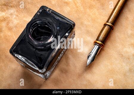 Calligraphy, letteratura e concetto creativo di scrittura con primo piano su una penna di quill di piuma e bottiglia nera di inchiostro su carta vecchia giallita o papiro Foto Stock