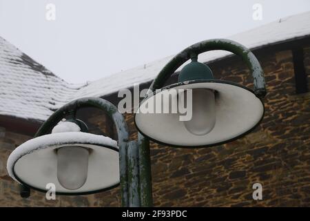 Lampada da strada con due lanterne in inverno di cui una è coperto di neve di fronte ad un edificio con un tetto innevato Foto Stock