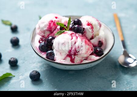 Yogurt fatto in casa e gelato al mirtillo con sciroppo di mirtillo naturale in una ciotola su sfondo blu ruvido Foto Stock