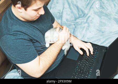 Giovane uomo con gattino che lavora al suo laptop. Il concetto di apprendimento online e di lavoro durante una pandemia. Foto Stock
