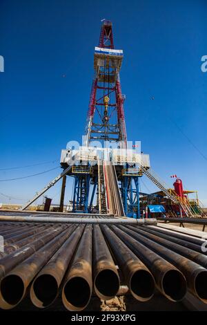 Regione di Aktobe, Kazakistan. Estrazione dell'olio dal deposito nel deserto con carro di perforazione. Tubi di perforazione, derrick e attrezzature su fondo azzurro chiaro cielo Foto Stock