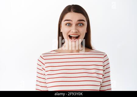 Immagine di ragazza entusiasta e sorpresa sentire stupende buone notizie, mascella goccia e stare stupito impressionato alla macchina fotografica, affascinato da qualcosa impressionante, in piedi Foto Stock