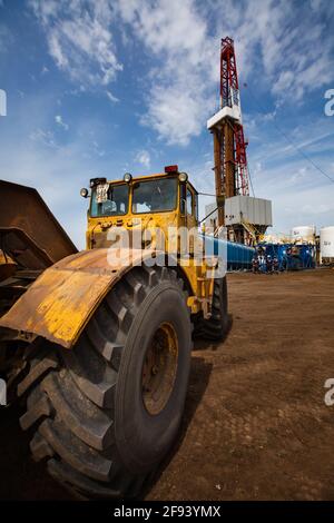 Regione di Uralsk, Kazakistan. Deposito di olio Zhaikmunai nel deserto. Carro di perforazione e attrezzature per la perforazione di petrolio. Trattore giallo in primo piano. Cielo blu con Foto Stock