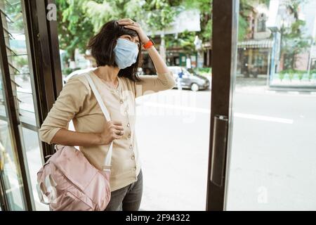 Donna asiatica che indossa una maschera sta aspettando l'autobus Foto Stock