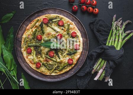 Flambee di tarte fatti in casa con asparagi verdi, pomodori e pesto all'aglio selvatico su un piatto di legno, vista dall'alto Foto Stock