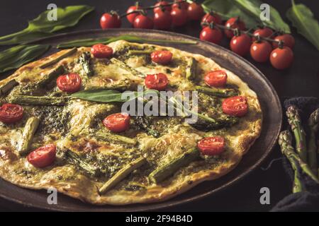 Flambee di tarte fatti in casa con asparagi verdi, pomodori e pesto su un piatto di legno Foto Stock