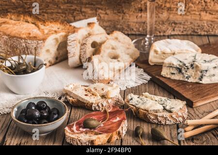 Crosta pane bianco francese con pancetta e formaggio e un ciotola con olive su tavola rustica in legno Foto Stock