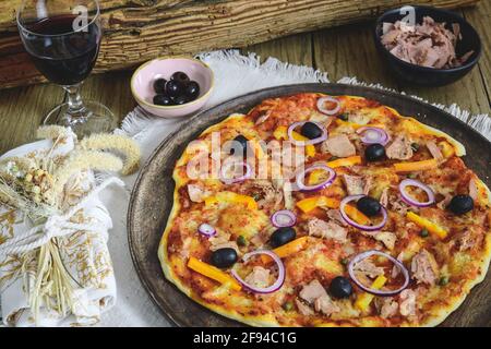 Gustosa pizza di tonno fatta in casa su un rustico tavolo di legno servita con vino rosso e olive Foto Stock