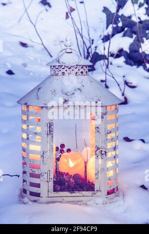 Lanterna bianca d'epoca con candele in un giardino innevato nella luce della sera, verticale Foto Stock