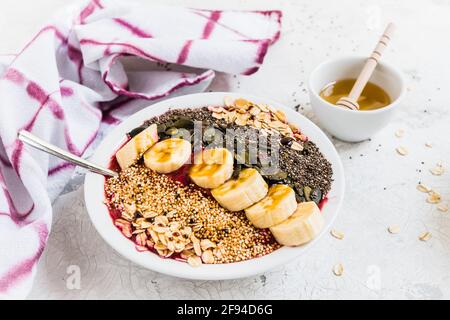 Colazione sana. Recipiente per frullato con mirtilli, banana, fiocchi di avena, semi di chia, quinoa, semi di zucca e miele. Foto Stock