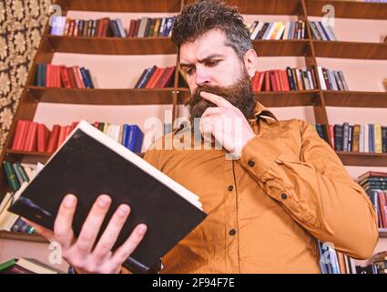 Uomo su occupato meditato libro di lettura del viso, librerie sullo sfondo. Concetto di educazione e scienza. Insegnante o studente con barba che studia in biblioteca Foto Stock